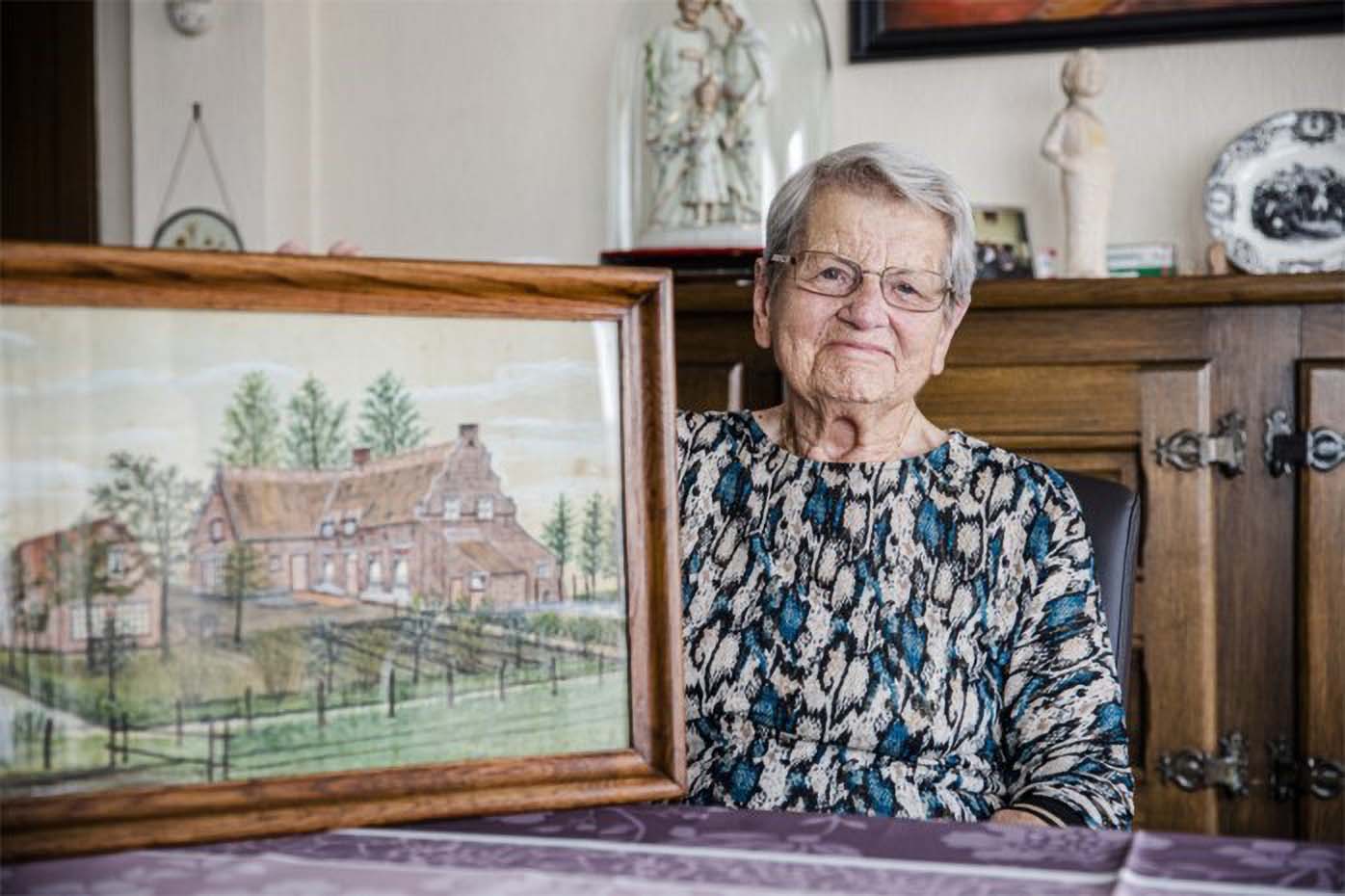 Bie Verlinden (93) next to a painting of the Brukel farmhouse that is featured in the game.